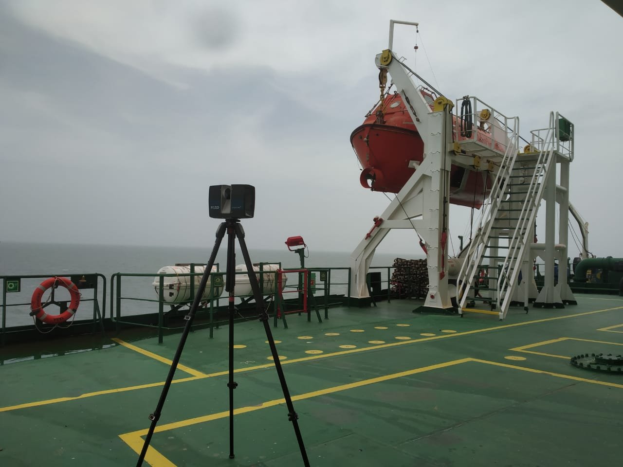 Tripod-mounted laser scanner on a ship deck beside a lifeboat platform