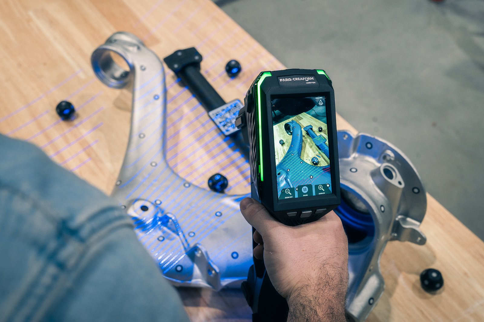 Handheld Creaform scanner capturing an automotive steering knuckle with blue scanning lines