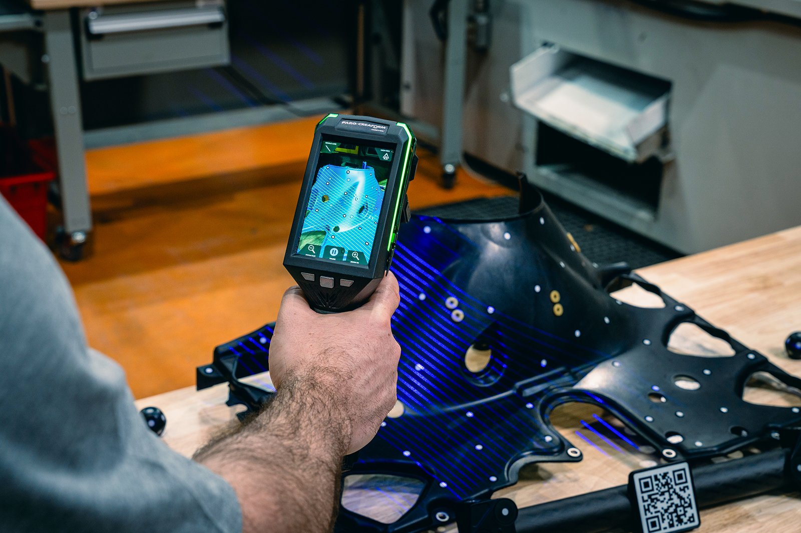 Creaform handheld scanner capturing a plastic automotive underbody panel with blue scanning lines